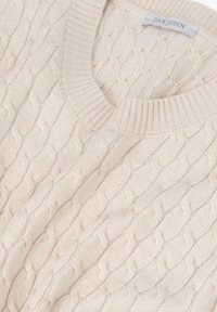 Suéter de punto en color crema con un cuello en V y puños acanalados. El patrón de punto incluye detalles texturizados en forma de ola a lo largo del tejido.