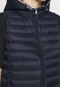 Granatowa pikowana kamizelka z zamkiem błyskawicznym z przodu, kapturem i przeszyciami. Posiada małe logo na lewej piersi oraz kontrastowe wykończenie wnętrza.