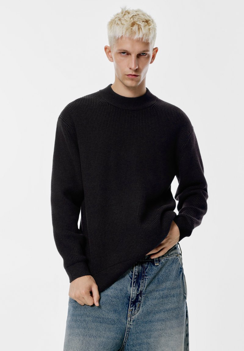 Maglione nero a costine con colletto alto e maniche lunghe, abbinato a jeans in denim azzurro chiaro con vestibilità comoda e una leggera texture.