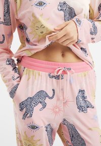 Světle růžový pyžamový set s vzorem leopardů, sluníček a očí, vyrobený z měkké látky s elastickým růžovým pasem a stahovací šňůrkou.