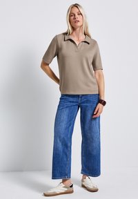 Beige poloshirt met kraag, korte mouwen, gecombineerd met wijde blauwe spijkerbroek en crèmekleurige sneakers. Casual, comfortabele stijl.