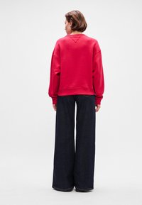 Sweatshirt rouge avec des épaules tombantes, des poignets côtelés et un ourlet arrondi, associé à un jean en denim foncé à jambes larges. Vue arrière de la tenue.