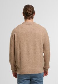 Maglione beige a maglia con orlo e polsini a coste. Presenta un collo rotondo e una vestibilità morbida, realizzato in un materiale morbido e testurizzato.