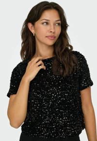 Schwarzes Paillettenoberteil mit Rundhalsausschnitt, kurzen Ärmeln und lockerer Passform; präsentiert eine strukturierte Oberfläche aus überlappenden Pailletten.