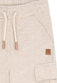 Beige Sweatpants mit elastischem Bund, weißen Kordeln, Seitentasche und einem kleinen braunen Etikett mit der Aufschrift "HUST and CLARE" auf der rechten Seite.