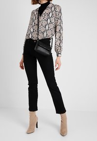 Blusa beige con stampa a serpente e scollo a V, abbinata a jeans neri aderenti e stivali beige con tacco alto. Inclusa una piccola borsa a tracolla nera.