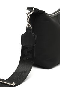 Černá nylonová taška přes rameno s hladkým povrchem, která má odnímatelný popruh s embosovanými detaily a stříbrný zip.