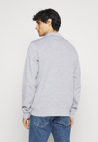 Gray sweatshirt with a soft texture, featuring a collared neckline, long sleeves, and a relaxed fit. Paired with blue denim jeans.