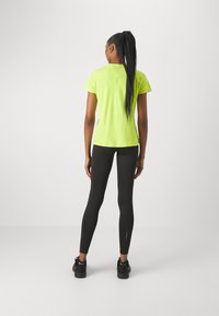 Camiseta deportiva amarilla neón de manga corta, combinada con leggings negros de corte ajustado y detalles reflectantes.
