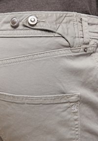 Los pantalones de algodón de color gris claro cuentan con una cremallera, cierre a presión y un bolsillo trasero con detalles de costura. Textura suave con un diseño ajustado.