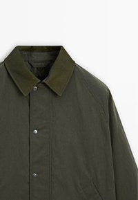 Groene jack met een kraag, drukknopen en een gestructureerde afwerking. Voorzien van raglanmouwen en zijzakken.