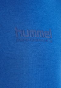Blåt stof med præget "hummel PERFORMANCE" tekst centreret, der fremhæver sportstøjsbranding på tekstureret tekstilmateriale.