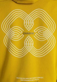 Gul stof med et abstrakt hvidt geometrisk design, ordet "CHASIN'" i midten, og lille hvid tekst nedenfor om komfort og ydeevne.