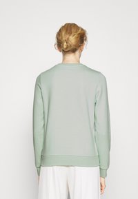 Sudadera verde claro con cuello redondo, mangas largas y dobladillo acanalado. Tela suave con detalles sutiles de costura en el escote.