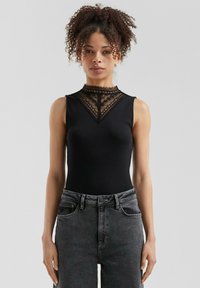 Bodysuit negro con un alto cuello de encaje y un intrincado detalle de encaje en el pecho, combinado con jeans oscuros de talle alto.