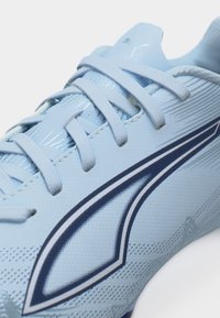 Svetlo moden športni čevelj z usklajenimi vezalkami, temno modrim logotipom na strani in teksturiranim zgornjim sintetičnim materialom.