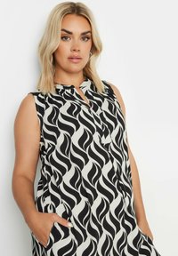 Hihaton musta-valkoinen mekko, jossa on aalto-kuvio, kaulus ja taskut. Kevyt kangas, jossa on sileä rakenne.