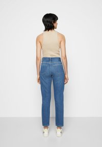 Blue denim jeans with a straight cut, two back pockets, and a medium rise, paired with a beige sleeveless top and white sneakers.