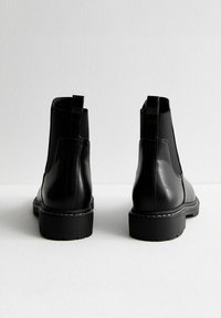 Czarne skórzane botki za kostkę z elastycznymi panelami po bokach i pętelkami do zakładania. Gruba podeszwa z białym przeszyciem, gładka faktura i zaokrąglony nosek.