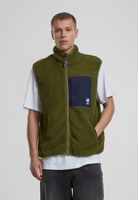 Grüner Fleece-Weste mit hohem Kragen, Frontreißverschluss, dunkelblauer Tasche mit Logo, zwei Seitentaschen und weichem, strukturiertem Gewebe.