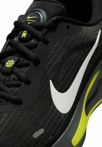 Czarne sportowe buty z teksturowaną cholewką, z szarymi i zielonymi akcentami, wyraźnym białym logo Nike oraz amortyzującą podeszwą.