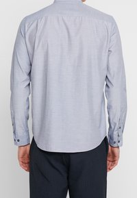 Ljusblå långärmad skjorta i texturerad tyg, med rak bakkjol och knappmanschetter, som har rundad nederkant och subtila sömmar.