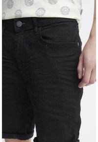 Sorte denimshorts med en let falmet tekstur. Har en knap- og lynlåslukning, fem lommer og oprullede kanter.