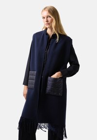 Námorní fleecová vesta s pro šívanými kapsami, knoflíkovým zapínáním a třásňovým lemem. Má uvolněný střih a jemnou texturu.