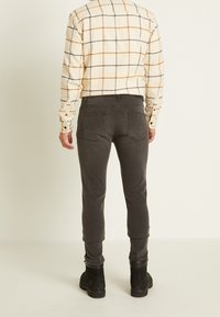 Miesten flanellikuvioinen paita, jossa on kerma- ja oranssiraidat, yhdistettynä tummanharmaisiin slim fit -farkkuihin ja mustiin nilkkakenkiin.