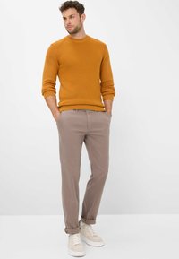 Pull en tricot orange avec un col rond, assorti à un pantalon beige clair et des baskets crème. Texture lisse avec des manches retroussées.