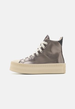 Hoge sneaker met glanzende grijze bovenzijde, witte veters, beige platformzool en zwarte hieltab op een witte achtergrond.