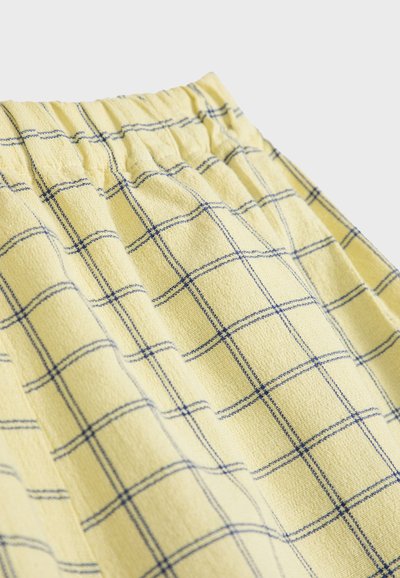 Tissu jaune à motif à carreaux bleus avec une ceinture élastique, montrant la texture et les détails de couture froncée.