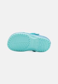Mėlynos žalios spalvos slip-on tipo batai su tekstūruota guma padu, reguliuojama dirželiu ir blizgančiu paviršiumi viršuje.