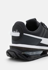 Black Nike sneaker featuring a textured fabric upper, white accents, a pull tab, and a visible air cushioning unit in the heel.