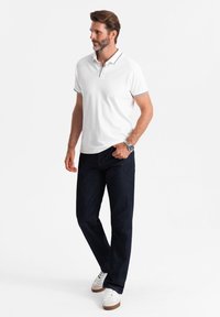 Vit polo skjorta med krage och marinblå detaljer, tillsammans med mörkblå jeans och vita sneakers med bruna sulor. Avslappnad passform och design.