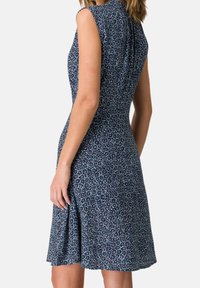 Une robe sans manches bleu marine avec un motif floral, présentant un corsage ajusté, une jupe évasée et des plis discrets au niveau du col.