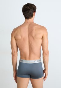 Bóxer gris con una suave cinturilla elástica que presenta el logo "Calvin Klein" en plata. Diseño ajustado con una textura suave.