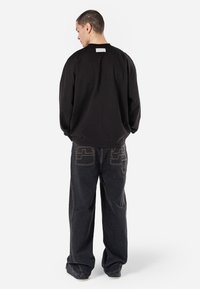 Sweatshirt noir oversize en coton, avec un col rond et une étiquette au dos. Associé à un jean en denim foncé avec des coutures contrastantes.