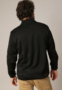 Zwarte langmouwpullover met een hoge kraag. Heeft een gestreepte stof en raglanmouwen, met een relaxte pasvorm en zonder zichtbare logo's.