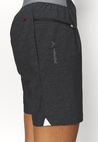 Tmavě šedé atletické šortky vyrobené z texturované látky, s postranní kapsou na zip, logem a bílým trojúhelníkovým akcentem na lemu.