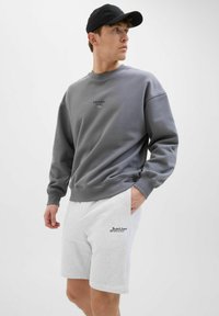 Sudadera gris con cuello redondo y texto bordado, combinada con pantalones cortos blancos con un logo, fabricados en una suave mezcla de algodón.