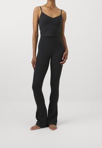Czarny, dopasowany crop top z cienkimi ramiączkami zestawiony z wysokimi spodniami dzwonami, oba wykonane z gładkiego, elastycznego materiału.