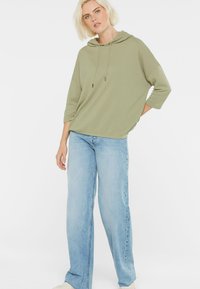 Olive green striped hoodie with a relaxed fit and drawstring, paired with light blue wide-leg jeans and white sneakers.