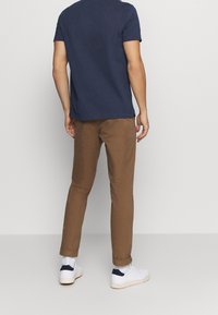 T-shirt bleu marine à manches courtes associé à un pantalon slim marron et des baskets blanches avec une accentuation marine, vu de dos.