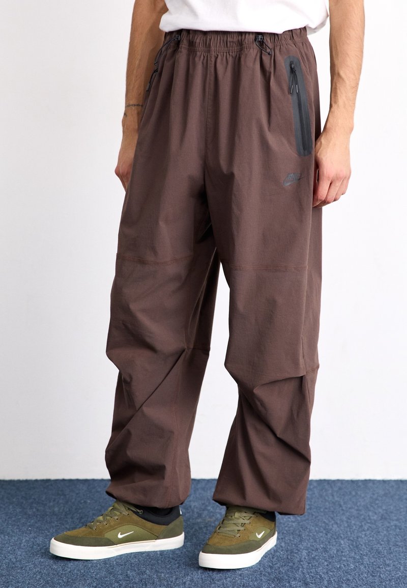 Bruna, lös passform byxor med elastisk midja och zip-ficka, tillverkade av lätt material. Kombinerat med olivgröna sneakers.