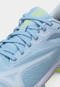 Κοντινό πλάνο ενός αθλητικού παπουτσιού σε ανοιχτό μπλε χρώμα με υφή από πλεκτό δίχτυ, κορδόνια στο ίδιο χρώμα, λευκές και νέον κίτρινες λεπτομέρειες και μαλακή ενισχυμένη σόλα.