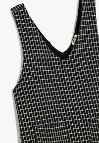 Vestido sin mangas a cuadros en blanco y negro con escote en V, tela texturizada y dos bolsillos frontales. El interior del escote es completamente negro.