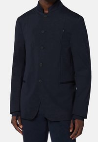 Marinblå blazer med ståkrage, sex knappar och sidofickor. Tillverkad av slät tyg med skräddarsydd passform och subtil lyster.