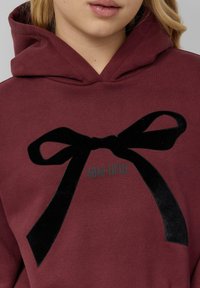 Bordowa bluza z kapturem z grafiką czarnej aksamitnej kokardy i napisem „BOW-TIFUL” w jasnym kolorze, o luźnym kroju i miękkiej fakturze.
