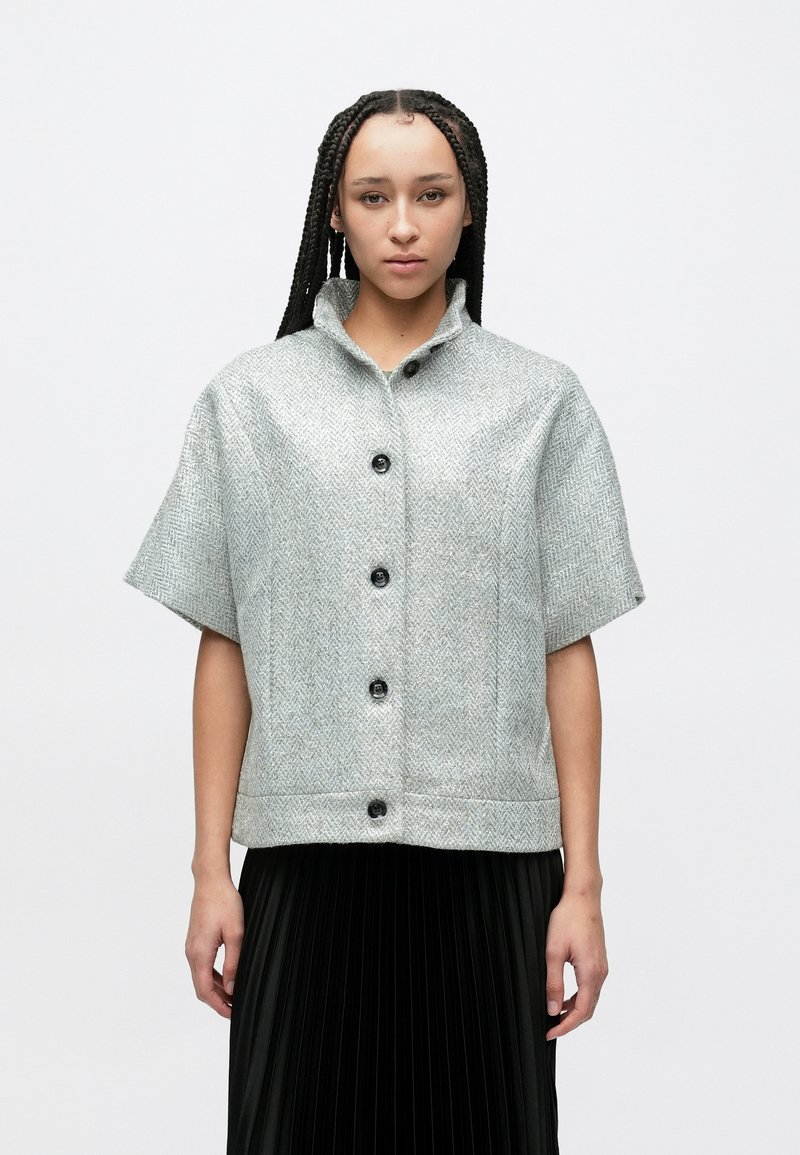 Kortærmet jakke med krave i et lysegråt fiskebenmønster, med sorte knapper og en lige nederste kant.